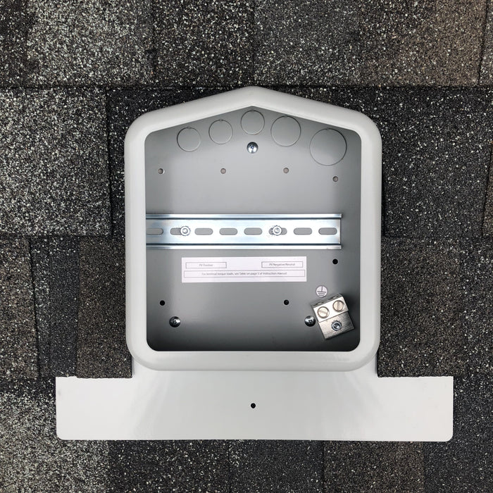 A rooftop mounting bracket for a solar panel installation is attached to a shingle roof. The Soladeck 0799-2G JB-1.XL Junction Box, featuring a rectangular shape, sturdy metal construction, and wiring holes, offers durability. The dark gray shingles have textured surfaces, ensuring a seamless integration.
