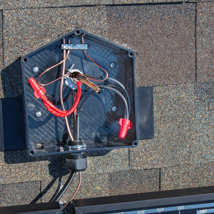 An open Ezsolar JB-1.2 Rooftop PV Junction Box from EZ Solar on a rooftop displays various wires and connectors. The dark brown shingles harmonize with a glimpse of solar panels at the bottom edge, ensuring water protection through its durable poly-carbonate construction.