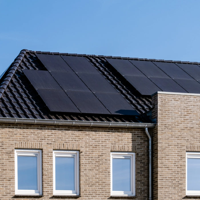 A brick house with SunPower 405W Solar Panels gleams under a clear blue sky. Four windows are visible on the second floor, nestled beneath the high-efficiency panels.