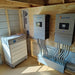 The image showcases an indoor setup with two Sol-Ark electrical units mounted on a wooden wall, intricately connected by multiple cables to the HomeGrid BMS and Base HG-MC100-200M2 floor unit by HomeGrid. This modular energy storage solution is ideal for off-grid cabins, situated in a room with partially unfinished interiors and visible insulation.