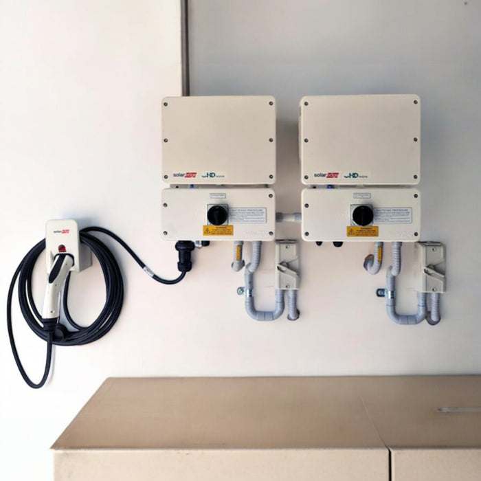 Two Solartek SolarEdge HD Wave Inverter 5kW units with coiled cables are mounted on a wall, featuring a control panel and integrating seamlessly with Home Wave tech for dual charging. The clean, organized area is perfect for indoor or garage use.